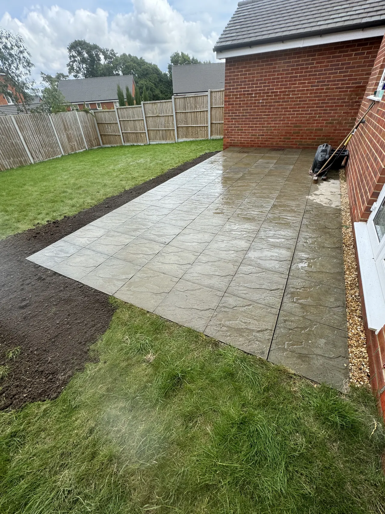 Large-format slab patio beside a red brick house with new turf