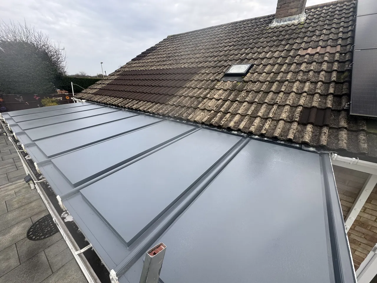 Grey fibreglass flat roof on a single-storey extension beside a tiled main roof