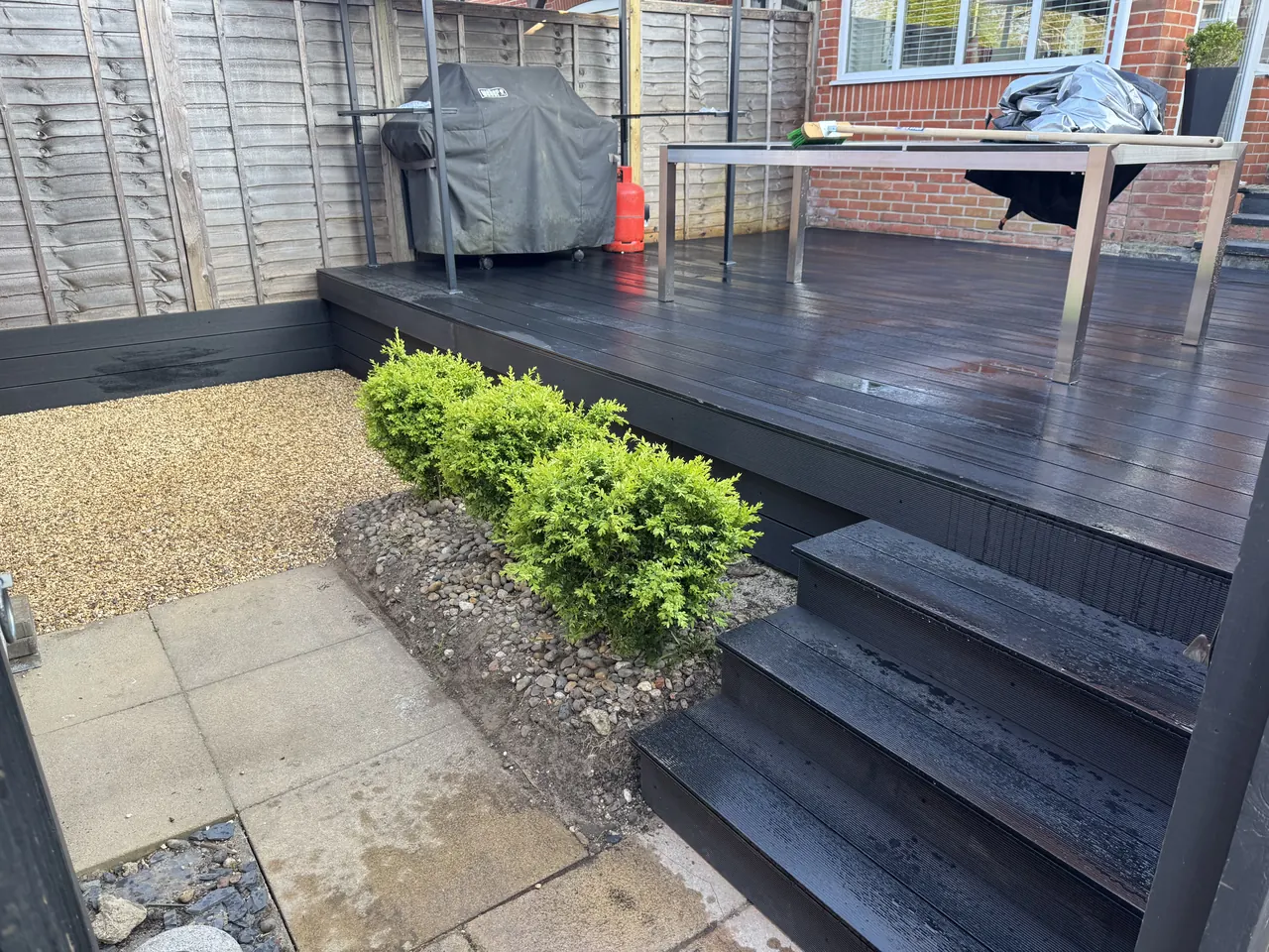 Dark composite decking with a stepped edge, gravel bed and box hedging