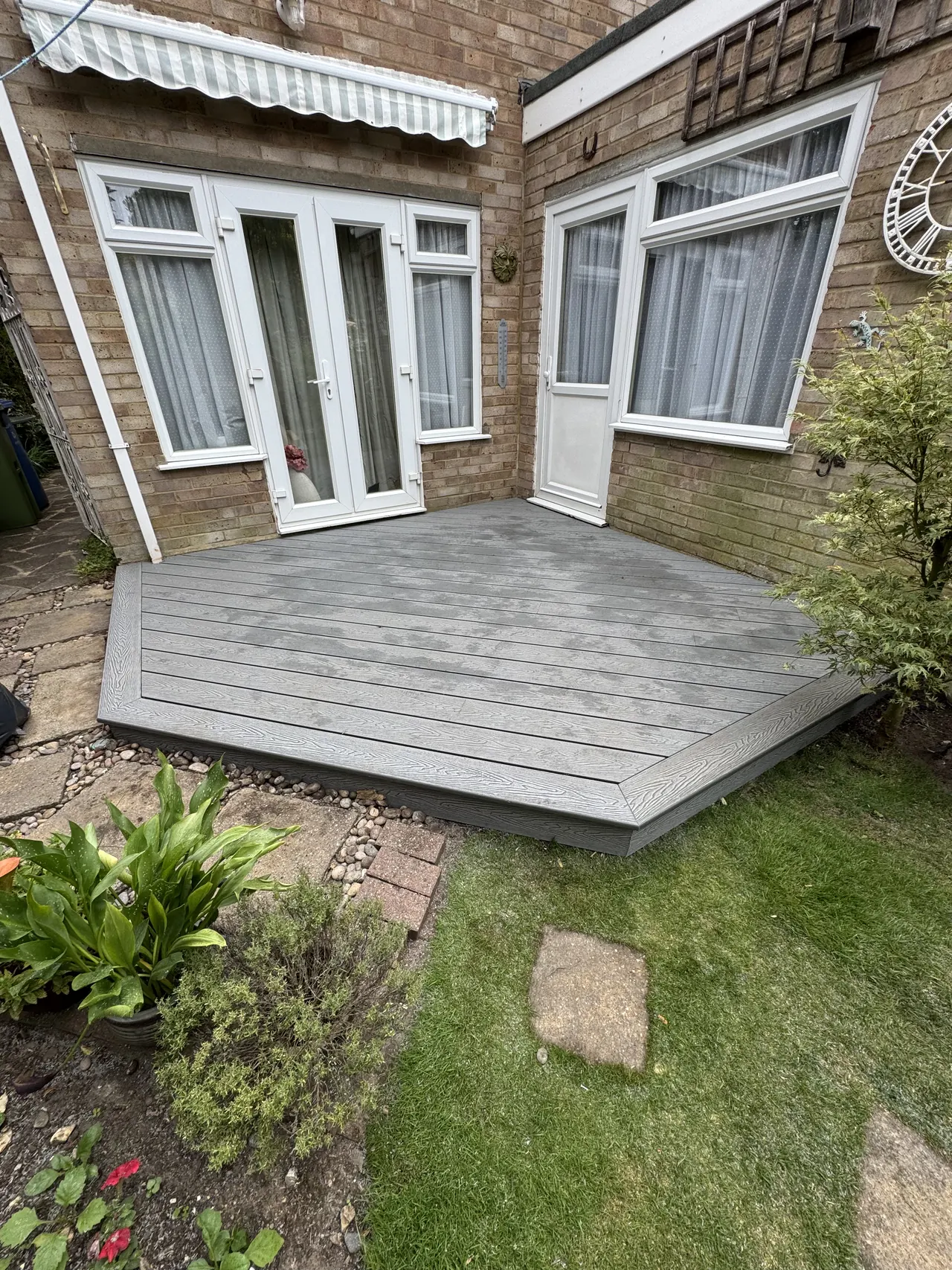 Grey composite decking cut to an octagon outside French doors on a brick bungalow