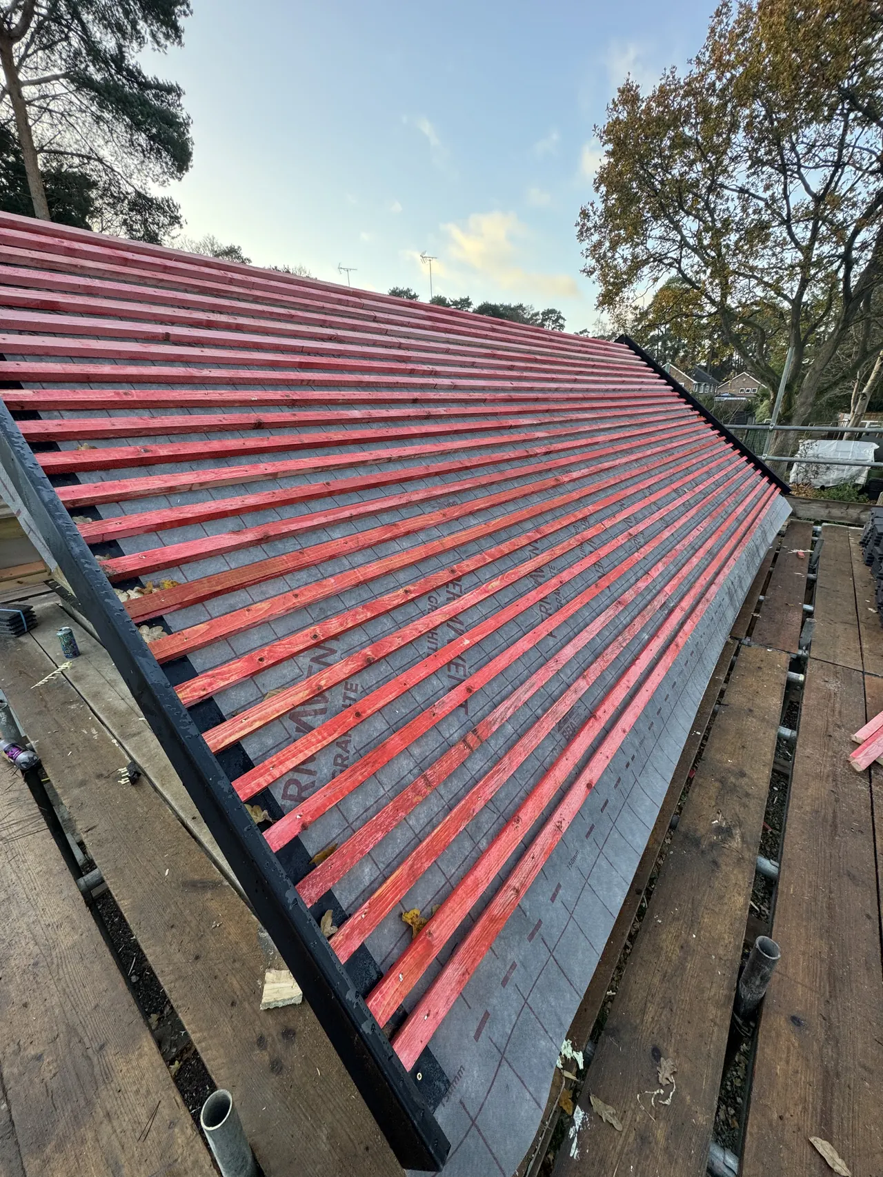 Red-treated timber battens over membrane on a new extension roof, scaffold boards below