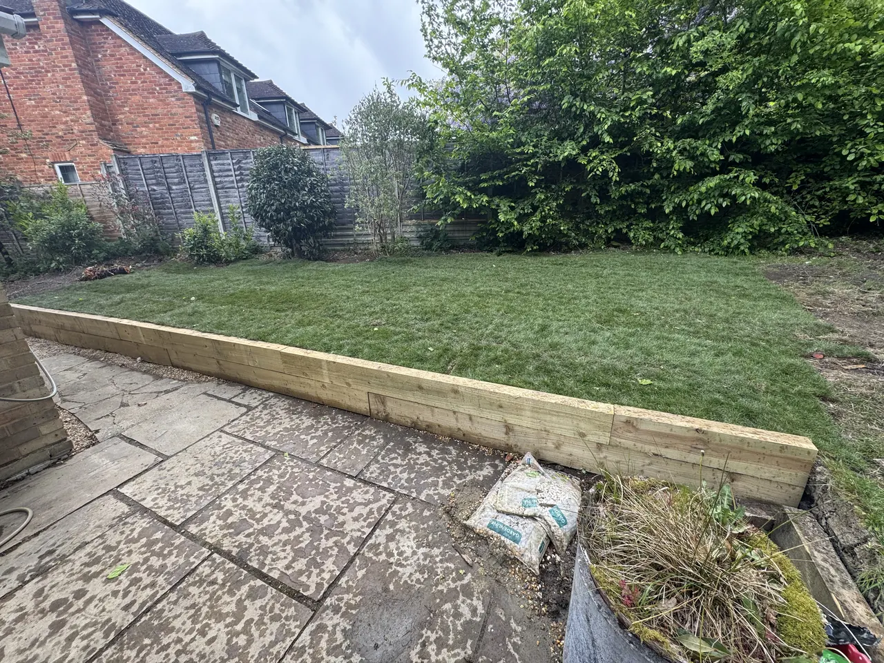 Timber sleeper retaining wall holding a lawn above a slab patio
